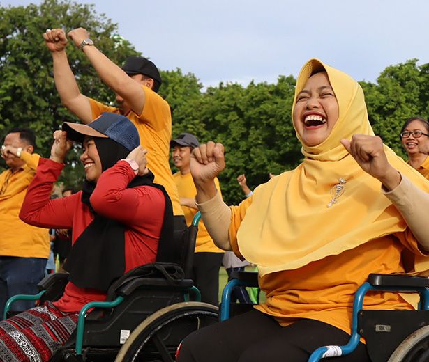 Group of excited people in Indonesia, including those living with disabilities, outdoors, pumping their fists in the air. Credit: INKLUSI